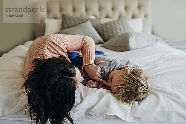 Glückliche Mutter spielt mit ihrem Sohn  während sie zu Hause im Bett liegt