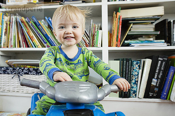 Porträt eines kleinen Jungen auf einem Spielzeug-Motorrad gegen heimische Bücherregale