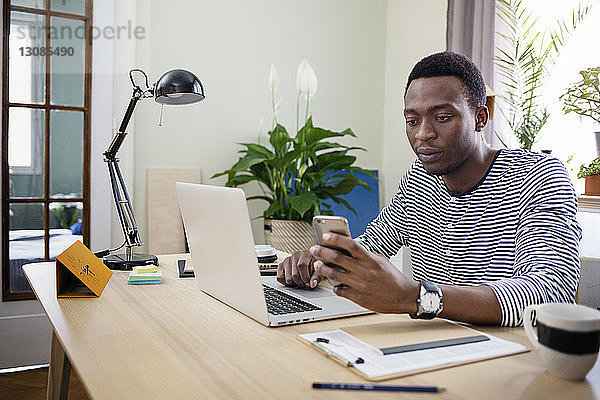 Junger Mann benutzt Smartphone bei der Arbeit zu Hause