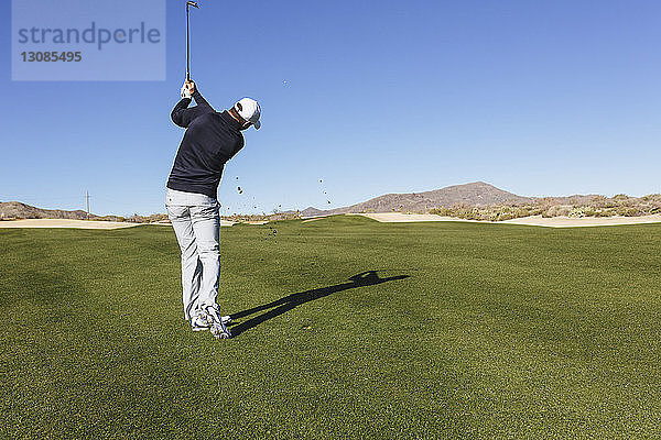 Rückansicht eines Golfspielers  der auf dem Feld gegen einen Golfspieler bei strahlend blauem Himmel spielt