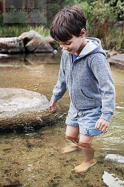 Glücklicher Junge steht im Wasser am Bach