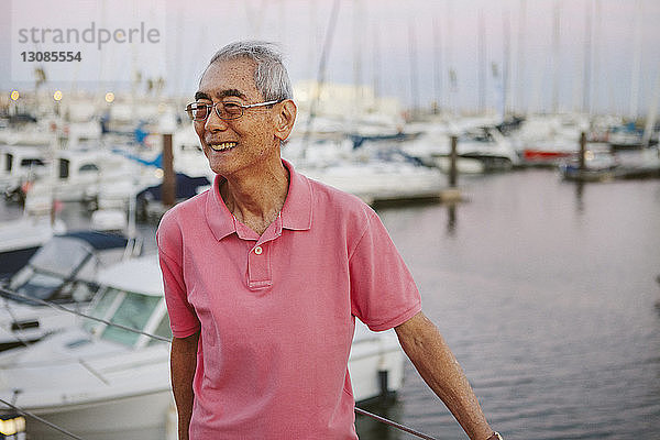 Lächelnder älterer Mann steht bei Sonnenuntergang vor im Hafen vertäuten Booten