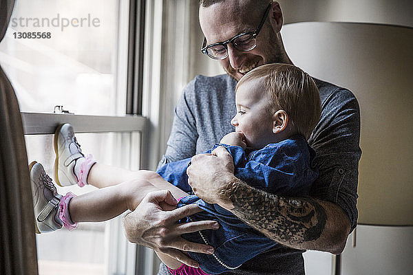 Glücklicher Vater trägt Tochter  während er zu Hause am Fenster steht