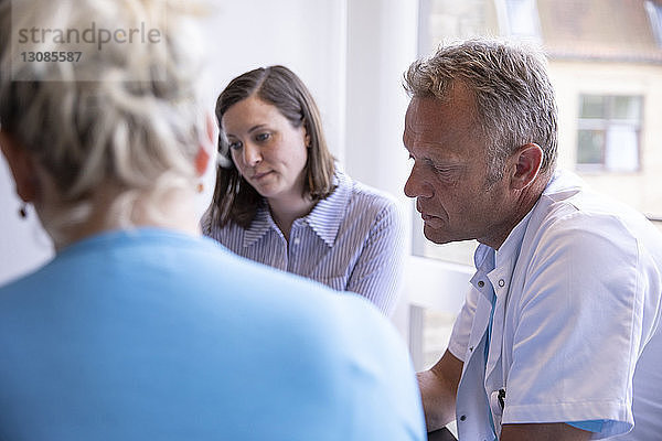 Ärzte sprechen mit Patientin  während sie in einer medizinischen Klinik sitzen