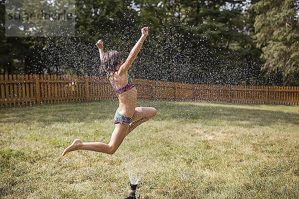 Fröhliches Mädchen springt im Hof über Sprinkler