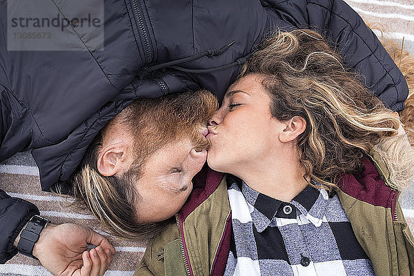 Draufsicht auf ein Paar  das sich küsst  während es auf einer Decke liegt