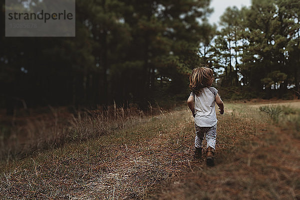 Rückansicht eines kleinen Mädchens  das auf einem Feld gegen Bäume läuft