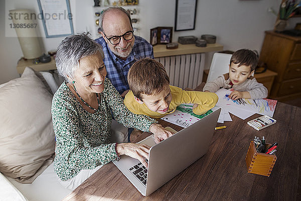 Hochwinkelansicht glücklicher Großeltern und Enkel mit Laptop zu Hause