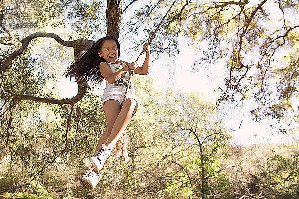 Fröhliches Mädchen spielt auf der Seilschaukel im Wald