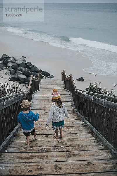 Schrägansicht von Geschwistern  die sich die Stufen hinunter zum Strand bewegen