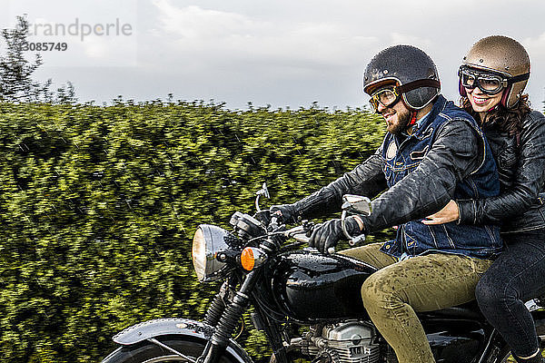 Glückliches Paar beim Motorradfahren durch Pflanzen gegen den Himmel