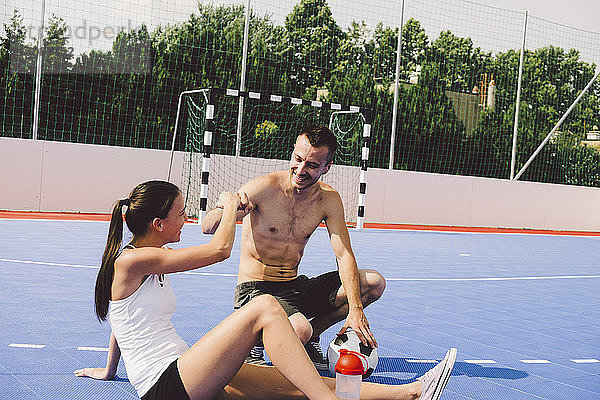 Junges Paar stößt bei sonnigem Wetter beim Fußballtraining auf dem Platz mit der Faust