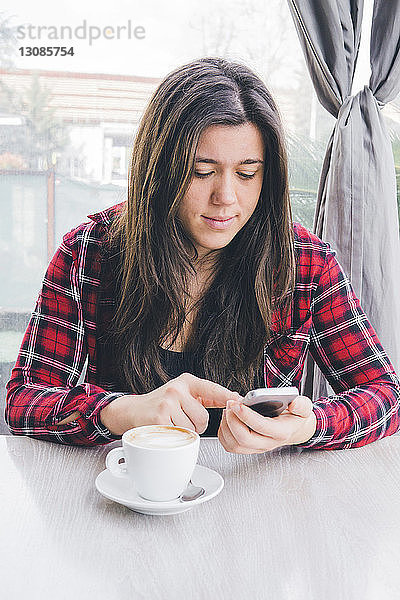 Frau mit Kaffee auf dem Tisch mit Smartphone gegen Fenster im Café