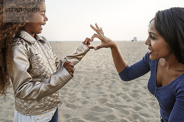 Mutter und Tochter bilden Herz mit der Hand am Strand