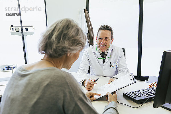 Glücklicher Arzt diskutiert mit Patient  während er im Krankenhaus an der Wand sitzt