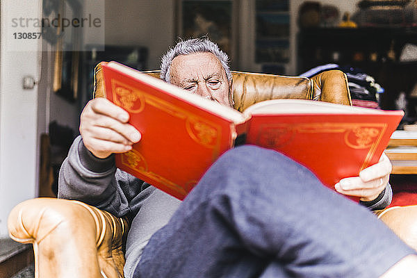 Niederwinkelansicht eines Mannes  der zu Hause auf einem Sessel sitzend ein Buch liest