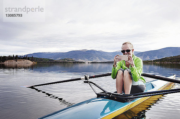 Glückliche Frau telefoniert beim Kajakfahren im See gegen den Himmel