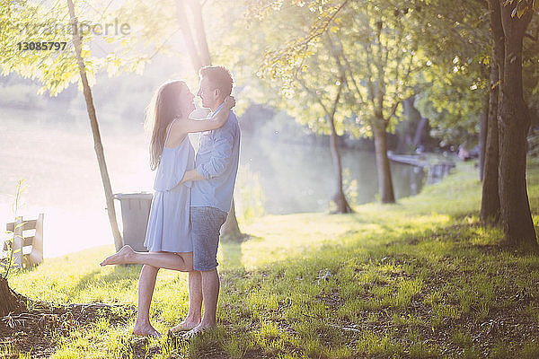 Seitenansicht eines romantischen Paares  das sich umarmt  während es auf einem Grasfeld im Park steht