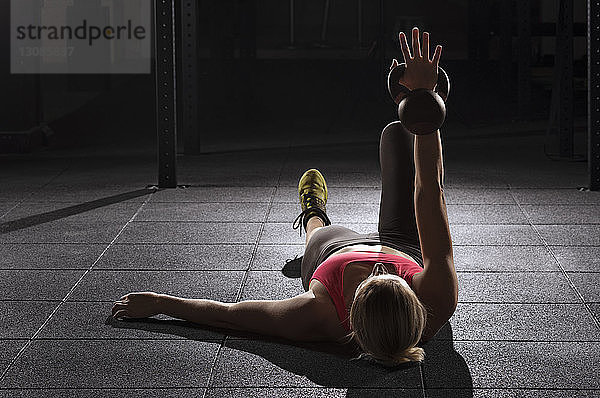 Weibliche Athletin hebt Kesselglocke  während sie im Fitnessstudio auf dem Boden liegt