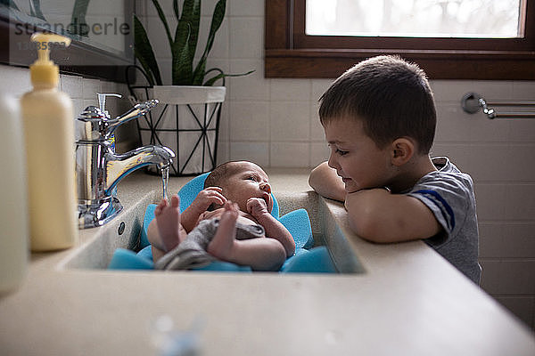 Bruder betrachtet zu Hause einen kleinen Jungen im Waschbecken im Badezimmer