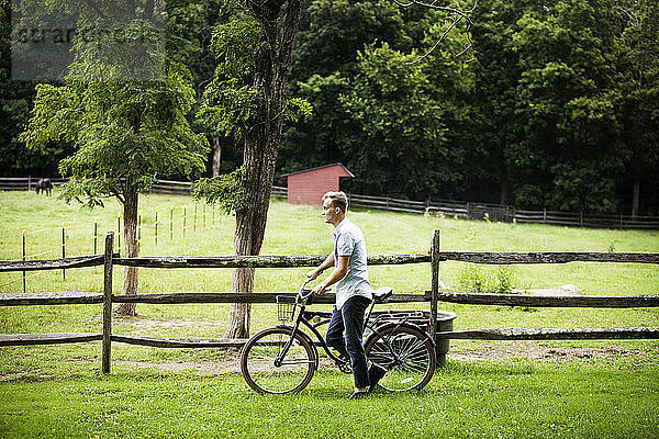 Mann mit Fahrrad zu Fuß am Zaun im Bauernhof