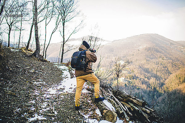 Rückansicht eines Wanderers mit Rucksack beim Fotografieren im Stehen auf dem Berg gegen den Himmel