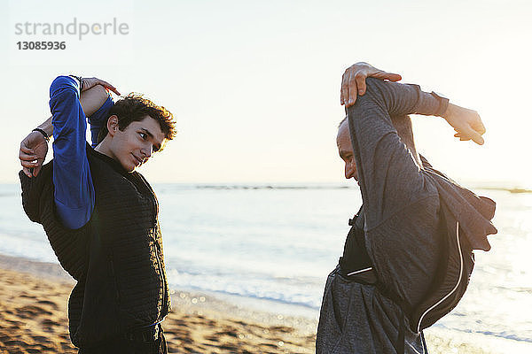 Vater und Sohn strecken die Arme aus  während sie am Strand mit dem Gesicht zum Himmel stehen