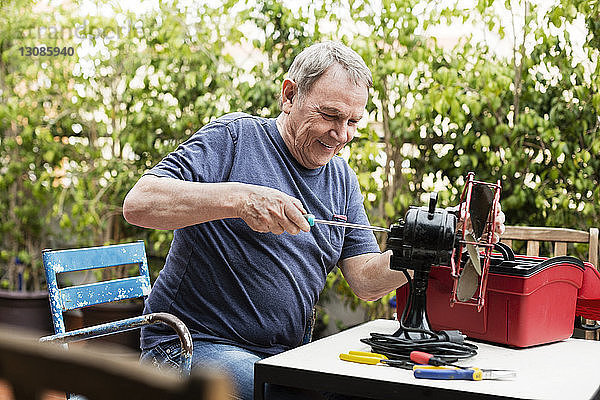 Glücklicher älterer Mann repariert elektrischen Ventilator auf dem Hof