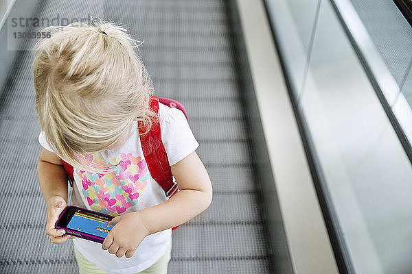 Hochwinkelansicht eines Mädchens  das ein Smartphone in der Hand hält  während sie auf dem Fahrsteig steht