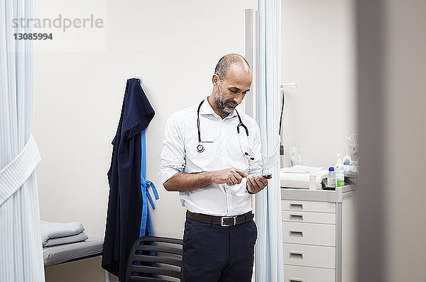 Arzt benutzt Smartphone  während er im Krankenhauszimmer steht und durch die Tür gesehen wird