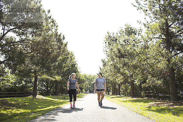 Mutter und Tochter in Sportkleidung gehen am sonnigen Tag auf dem Fußweg im Park spazieren