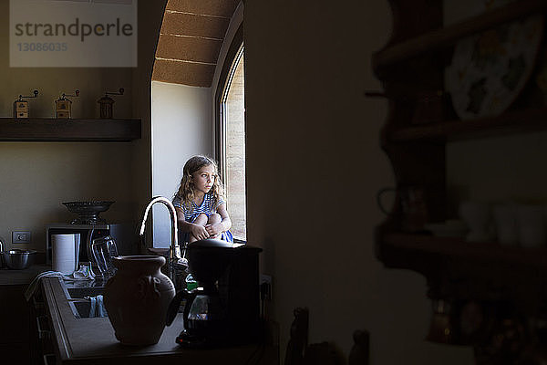 Mädchen  das durch ein Fenster schaut  während es zu Hause in der Küche sitzt