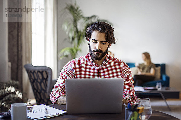 Kreativer Geschäftsmann  der am Laptop arbeitet  während er im Büro am Tisch sitzt