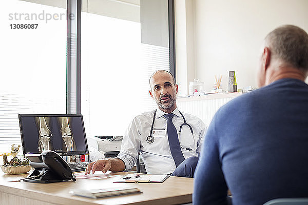 Arzt spricht mit Patient  während er im Krankenhaus am Schreibtisch sitzt