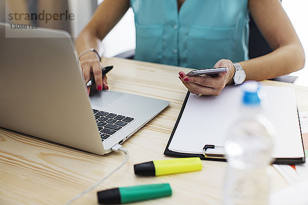 Mittendrin Geschäftsfrau mit Laptop und Smartphone am Schreibtisch