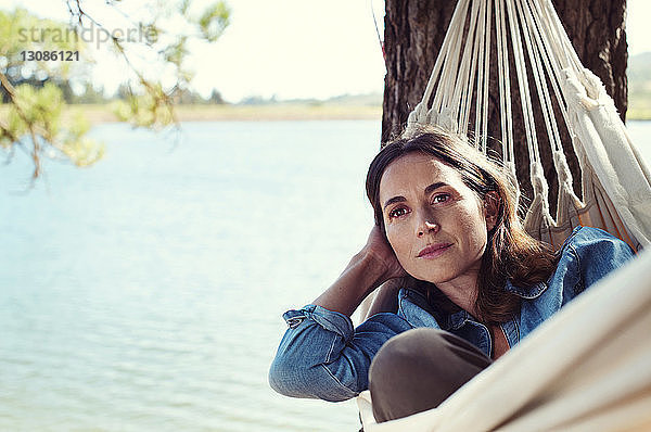 Nachdenkliche Frau schaut weg  während sie sich auf einer Hängematte am See entspannt