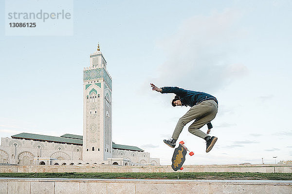 Seitenansicht eines Skateboard fahrenden Mannes gegen die Moschee Hassan II