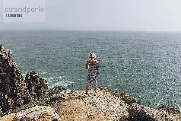 Frau in voller Länge schaut auf das Meer  während sie auf einer Klippe steht