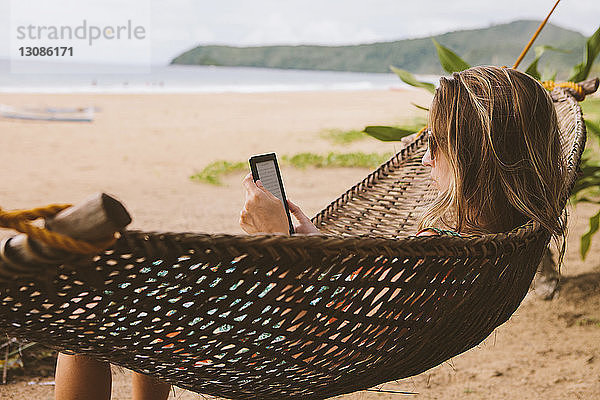 Frau benutzt Tablet-Computer  während sie sich auf Hängematte am Strand entspannt