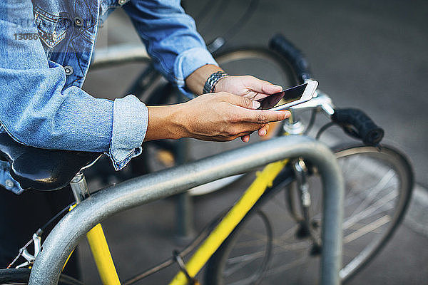 Abgetrennte Hände eines Mannes  der ein Smartphone mit dem Fahrrad benutzt