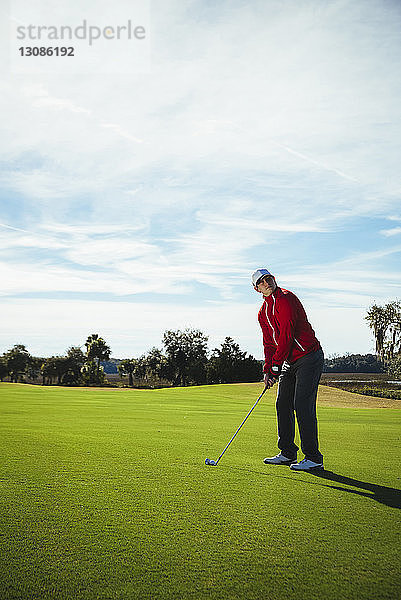 Ein Mann in voller Länge spielt Golf  während er auf dem Feld gegen den Himmel steht