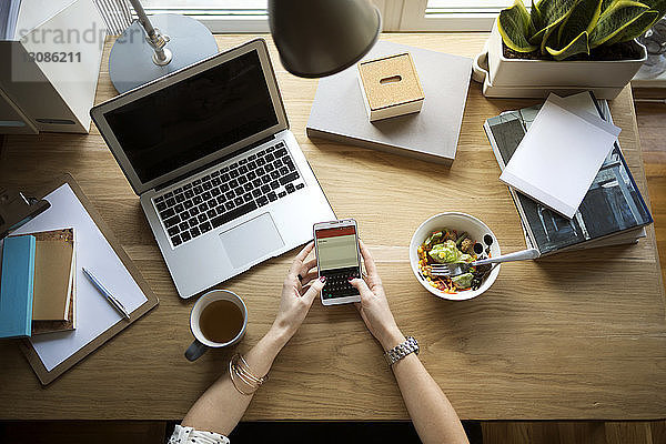 Draufsicht einer Frau  die ein Smartphone am Schreibtisch im Home-Office benutzt