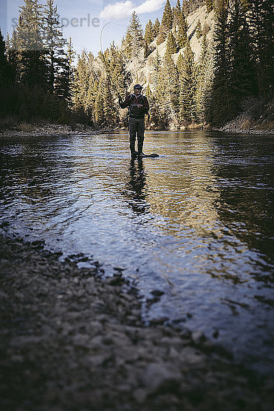 Mann angelt  während er im Fluss am Wald steht