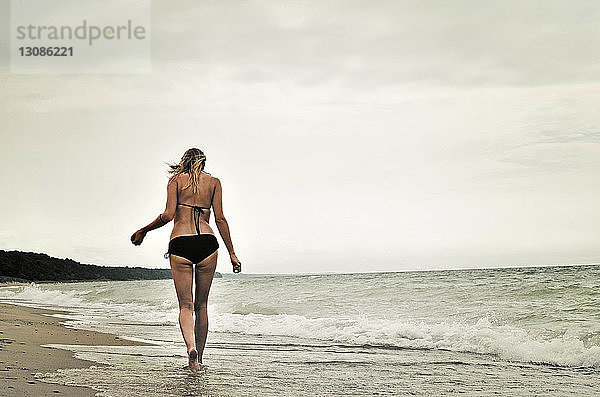 Rückansicht einer Frau im Bikini  die am Strand vor klarem Himmel spazieren geht
