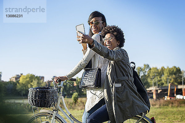 Glückliche Freunde  die beim Fahrradfahren auf dem Feld Selbsthilfe durchs Telefon nehmen