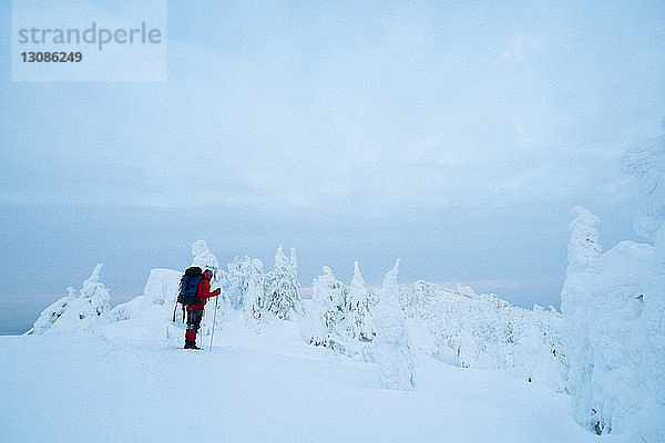 Seitenansicht eines Wanderers  der auf einer schneebedeckten Aufschüttung vor bewölktem Himmel steht