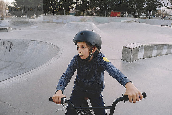 Junge mit Helm beim Sitzen auf dem Fahrrad im Skateboard-Park