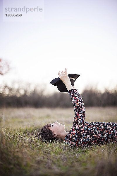 Junge Frau mit Hut in der Hand  während sie sich auf einem Grasfeld entspannt