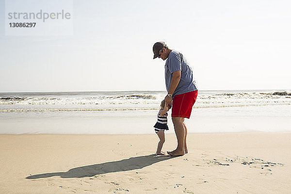 Vater und Tochter genießen am sonnigen Tag am Strand gegen den Himmel