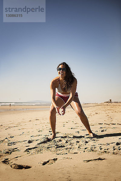 Volle Länge einer glücklichen Frau beim Volleyballspielen am Strand